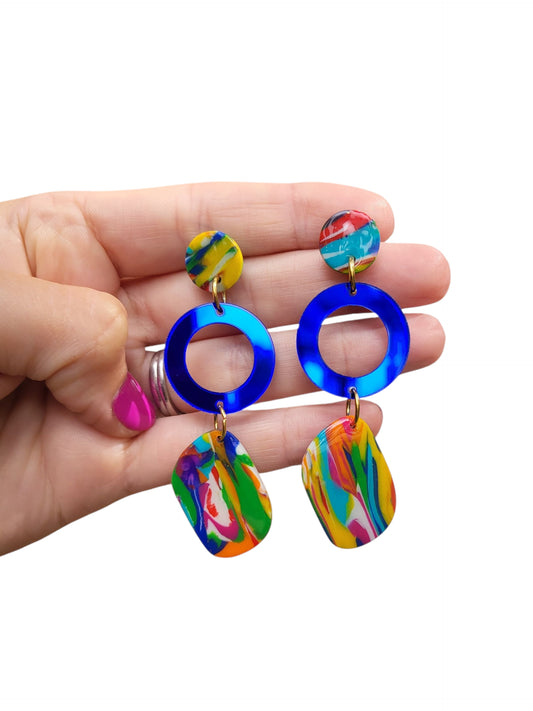 Make a bold statement with these unique, handmade earrings. Featuring a vibrant, abstract polymer clay earrings with splashes of yellow, pink, and turquoise, these earrings are complemented by a striking cobalt blue hoop and a small circular top piece. Lightweight and eye-catching, they are perfect for adding a pop of color to any outfit. Ideal for those who love artistic, contemporary jewelry.