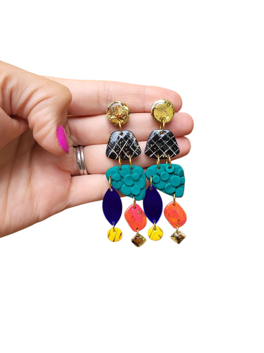 Boho Glam Dangling Statement Earrings 
The design features a captivating mix of shapes and textures, from the intricate, geometric pattern on the top to the bold, solid acrylic blue ovals and the brightly coral and pink colored abstract diamond shapes and gold derails. The vibrant, abstract design is a perfect way to add a pop of color to any outfit, making them an ideal boho statement